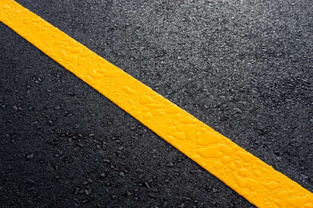 Close-up top view, new yellow stripe symbol texture background, wet with dew drops on a black asphalt road with early morning sunlight and darkness.の写真素材