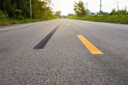 A close-up low-angle view. A long line of black rubber tires stopping violently against the paved road surface with yellow stripes are common in rural Thailand.の写真素材