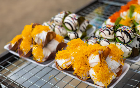 Close up, crispy Thai desserts filled with cream, sprinkled with yellow coconut husks and delicious chocolate in a dish placed on a stainless steel wire rack for sale in a Thai rural market.の写真素材