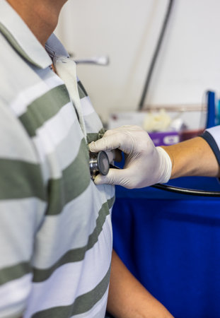 Close-up shot of doctor's hand doing auscultation of heartbeat and trachea with a device on a sick person to check and observe the symptoms of any disease or not.の写真素材