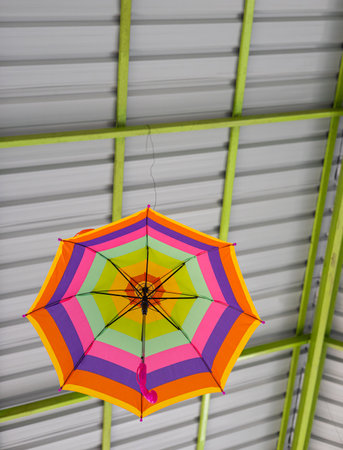 A low-angle view passes through a colorfully decorated umbrella hanging beneath a roof structure...