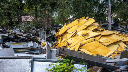 View of large piles of scraps of steel sheets and old yellow foam piled up to wait for reuse outside an antiques shop near a row of trees and Residential houses in one of the rural areas of Thailand.の写真素材