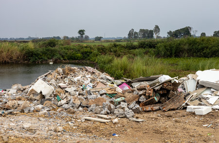 Scenery of piles of concrete debris and white tiled ceilings being dumped together as garbage piled up on the soil along the canal near the agricultural area, commonly seen in rural Thailand.の写真素材