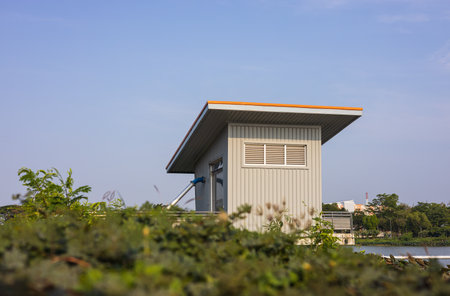 A low angle view through the grass to a blue zinc hut with water pipes installed as a water supply control room in a large well in rural Thailand.の写真素材