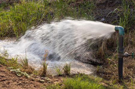 Close-up view of water gushing violently out of a water supply pipe installed in a well filled with...
