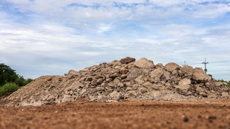 Low angle view of the demolished concrete road rubble piled on the ground, brown pebbles to fill with trees and cloudy clouds as a backdrop in the Thai countryside.の写真素材
