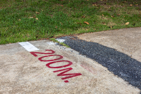 A low-angle, close-up view of red distance letters and white arrows sprayed onto the concrete, which forms a fitness path near the steel gratings and lawns of a park.の写真素材