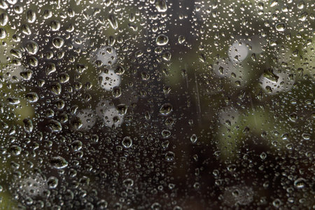 Close-up view of background texture, many rain drops outside the rear window of a car, looking at a blurred background, bokeh, green leaves in a Thai countryside during the rainy season.の写真素材