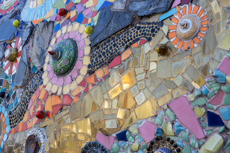 The background wall, which is made from colorful broken glass bowls and decorated with cement and stones, is contemporary art in an ancient temple in Thailand.の写真素材