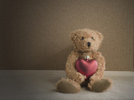 Teddy bear sitting with red heart on fabric and corkboard background. vintage styleの写真素材