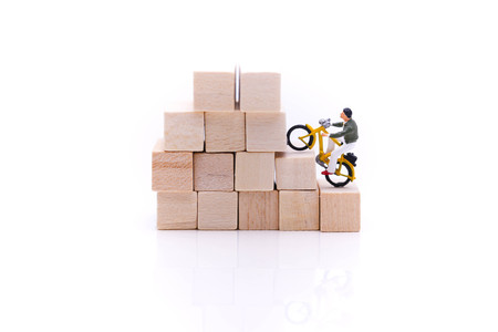 Miniature people : man ride bicycle on stack of wooden block.