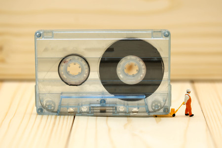 Miniature people : worker with Audio cassette with magnetic tape.