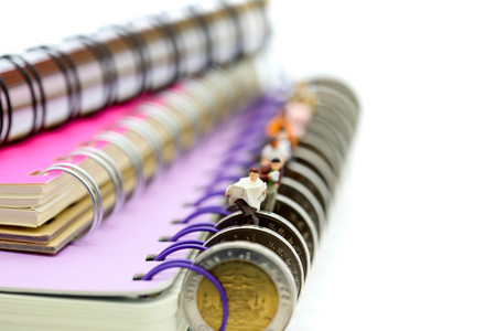 Miniature people: Businessman reading newspaper and sitting on book using as background education or business concept.の写真素材