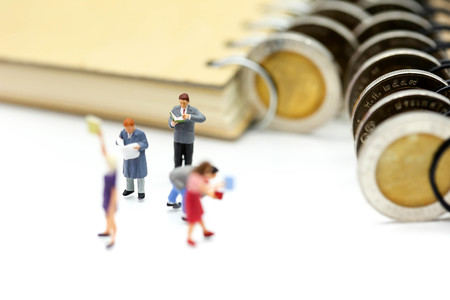 Miniature people: Businessman reading newspaper and sitting on book using as background education or business concept.の写真素材