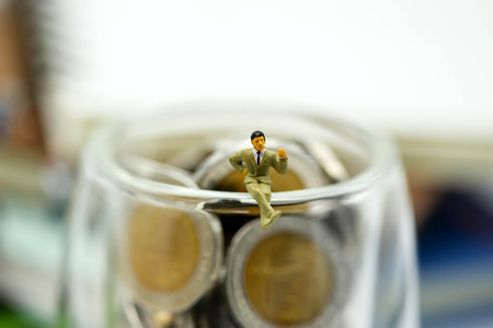 Miniature people : Businessman sitting on glass jar of coins.の写真素材