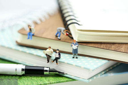 Miniature people: Businessman reading newspaper and sitting on book using as background education or business concept.の写真素材