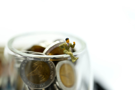 Miniature people : Businessman sitting on glass jar of coins.の写真素材