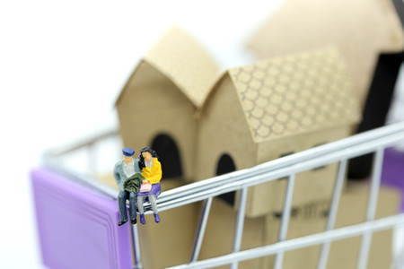 Miniature people : Couple sitting on Shopping Cart with mini house toy.の写真素材