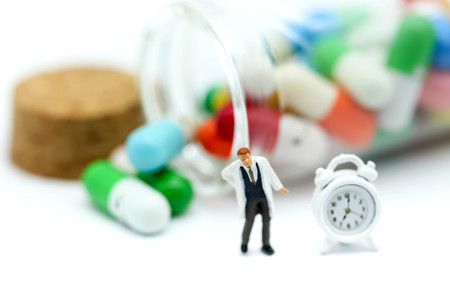 Miniature people : doctor stand with  drug and clock background,Health concept.の写真素材