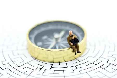 Miniature people :  businessman sitting on  compass with maze,Concepts of finding a solution, problem solving and challenge.の写真素材