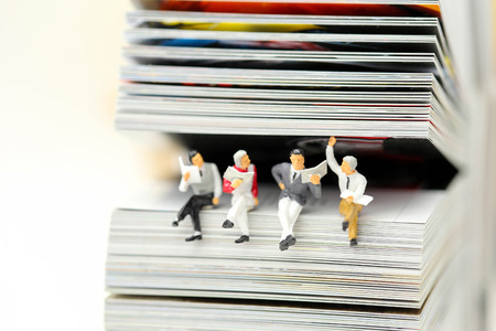 Miniature people: Businessman reading newspaper and sitting on book  using as education or relax business  concept.の写真素材
