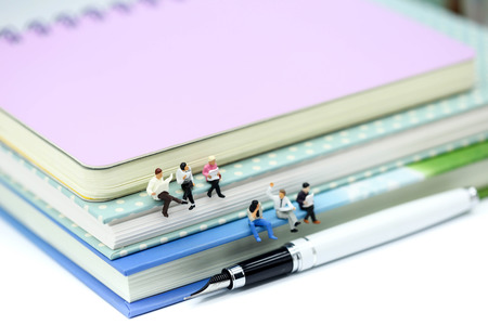 Miniature people: Businessman reading newspaper and sitting on book  using as education or relax business  concept.の写真素材