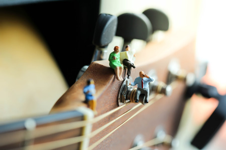Miniature people: Businessman reading newspaper and sitting on acoustic guitar,time of relax or music relax,stationary,business concept.の写真素材