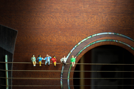 Miniature people: Businessman reading newspaper and sitting on acoustic guitar,time of relax or...
