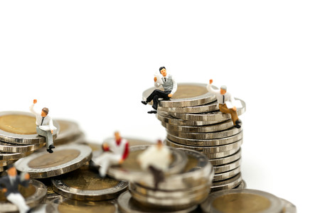 Miniature people:  businessmen sitting on coins and reading newspaper, book using as background...
