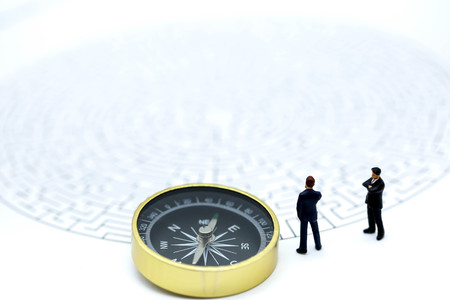 Miniature people: Businessman standing on start point of maze with compass , businessman making the right choice concept.の写真素材