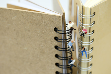 Miniature people: Businessman reading newspaper and sitting on book using as background education or...
