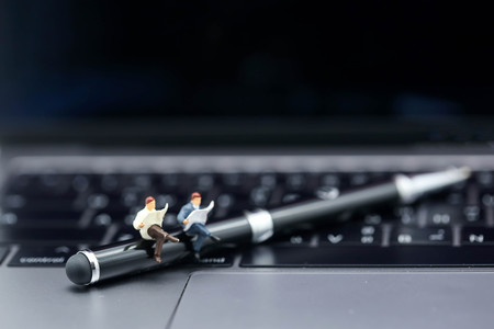 Miniature people : reading a book sitting on pen with laptop,education relax concept.の写真素材