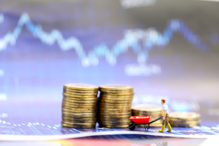 Miniature people : worker pulling stack coins with graph chart financial analysis review document.