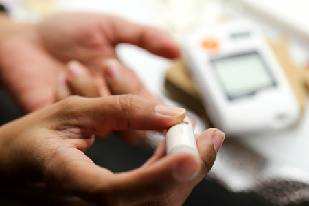 Close up of male finger with blood drop and test stripe to checking blood sugar level by Glucose...