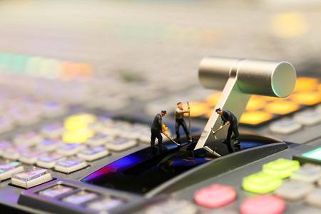 Miniature people : worker on Switcher buttons in studio TV station, Audio and Video Production...