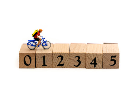 Miniature people : Travelers riding bicycle on wooden block number using as background traveling...