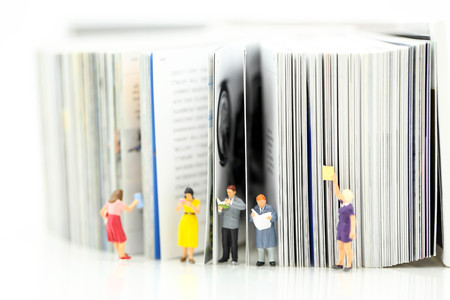 Miniature people: Businessman reading newspaper and sitting on book using as background education or business concept.の写真素材