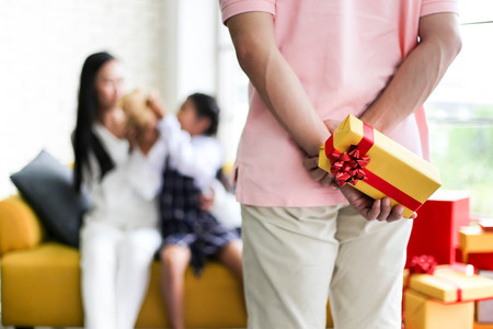 Man hiding gift for Parent and little child having fun near Christmas tree indoors behind his backの写真素材
