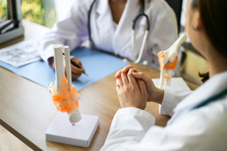 Beautiful woman Doctor is pointing on a bone in the spine the layout of the knee joint with patient.の写真素材