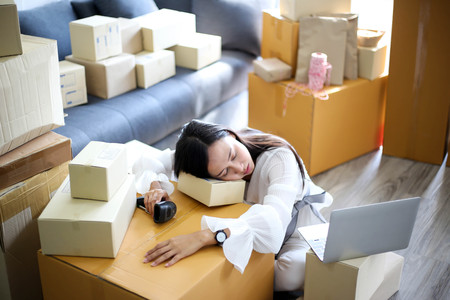 Tired unhappy of   Young asian girl is freelancer Start up small business owner writing address on cardboard box at workplace,Shipping shopping online small business entrepreneur SME or freelanceの写真素材