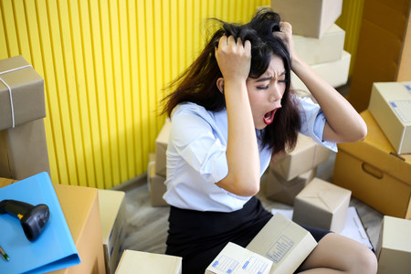 Tired unhappy of   Young asian girl is freelancer Start up small business owner writing address on cardboard box at workplace,Shipping shopping online small business entrepreneur SME or freelanceの写真素材