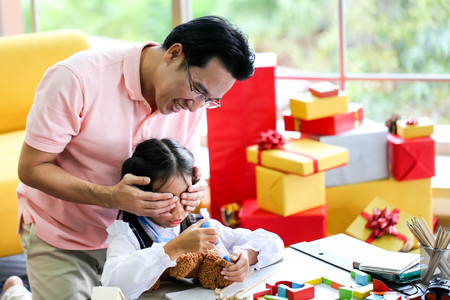 Man hiding gift for Parent and little child having fun near Christmas tree indoors behind his backの写真素材