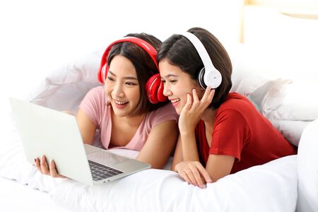 Happy Couple  asia woman wear headphones and enjoy musics playing mobile phone and tablet in bedroom.の写真素材