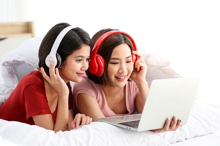 Happy Couple  asia woman wear headphones and enjoy musics playing mobile phone and tablet in bedroom.の写真素材