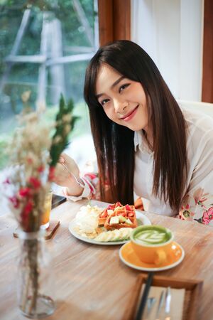 Beautiful asian woman eating delicious  waffles in coffee shop cafe.の写真素材