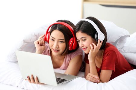 Happy Couple  asia woman wear headphones and enjoy musics playing mobile phone and tablet in bedroom.の写真素材