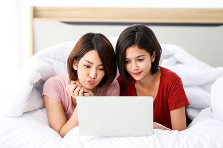 Happy young couple friend beautiful asia women lying on the bed in a bedroom and using digital tablet.の写真素材