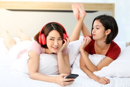 Happy Couple  asia woman wear headphones and enjoy musics playing mobile phone and tablet in bedroom.の写真素材