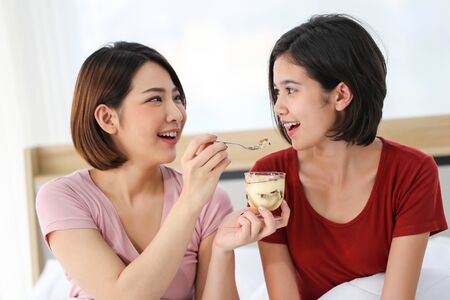 Happy young couple friend beautiful asia women enjoying cake together on the bed in bedroom.の写真素材