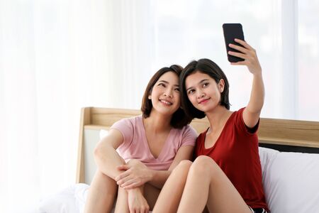 Couple friend beautiful asia woman together for selfie photo and snap by smartphone in white bedroom at house in the morning.の写真素材